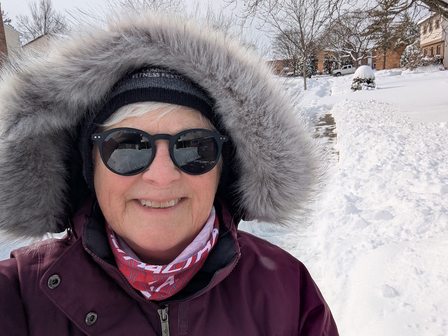 woman wearing purple coat and sunglasses walking in the snow.